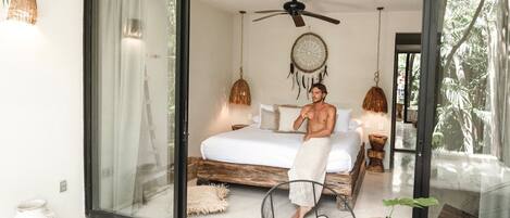 A bedroom with a large bed, a ceiling fan, a dreamcatcher, and a view of the outdoors.