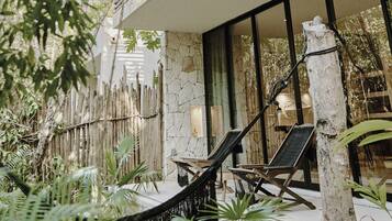 A hammock chair and a lounge chair in a tropical setting with a bamboo fence and lush greenery.
