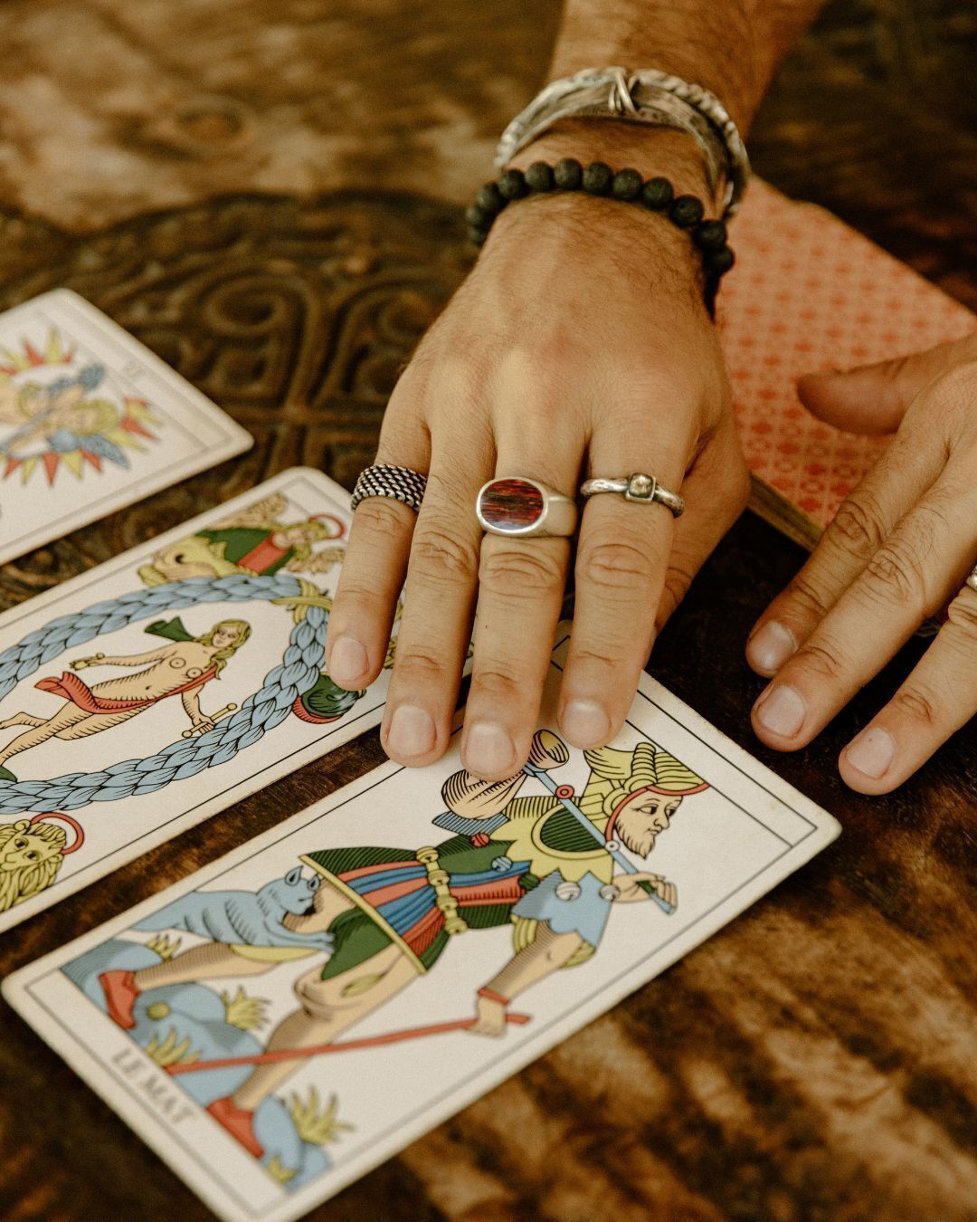En hand med flera ringar som ligger på tarotkort.