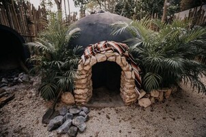 Une arche en pierre au style rustique, entourée de plantes tropicales et bordée d’un sol sablonneux.