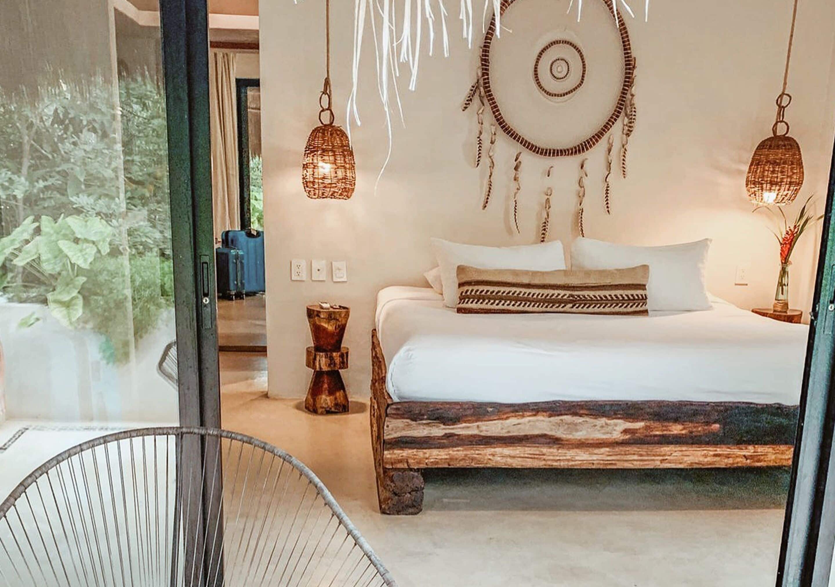 A bedroom with a bed, hanging dreamcatchers, and a view of greenery outside.