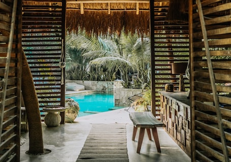 A pool area with a wooden deck, a bench, and a thatched roof structure.