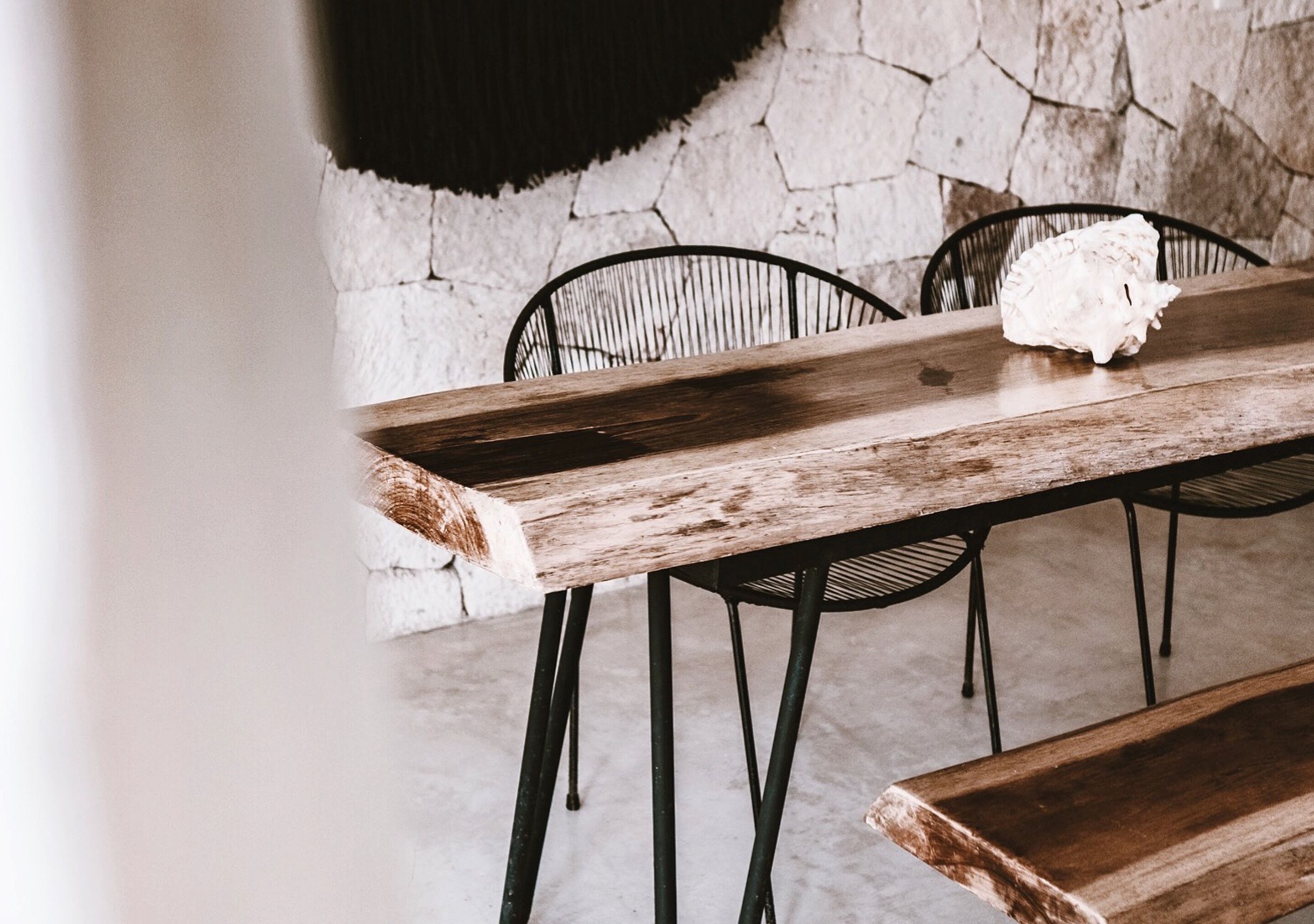 Una mesa de madera rústica con patas metálicas, junto con un banco, frente a una pared de piedra.