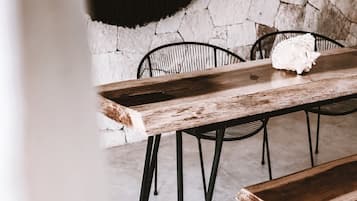 Una mesa de madera rústica con patas metálicas, junto con un banco, frente a una pared de piedra.