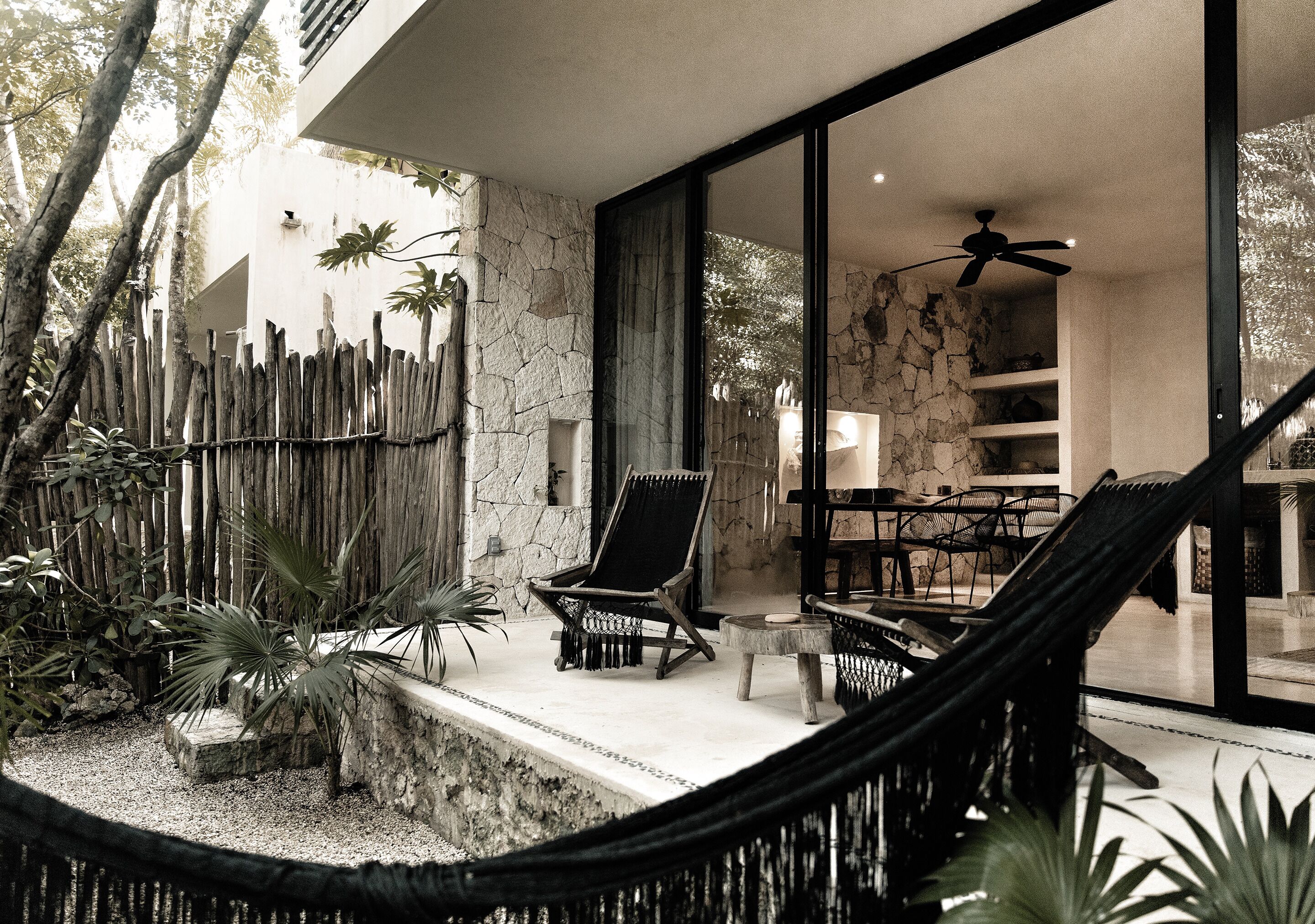 Un espace extérieur moderne aménagé avec des sièges, un hamac, des murs en pierre et des plantes tropicales.