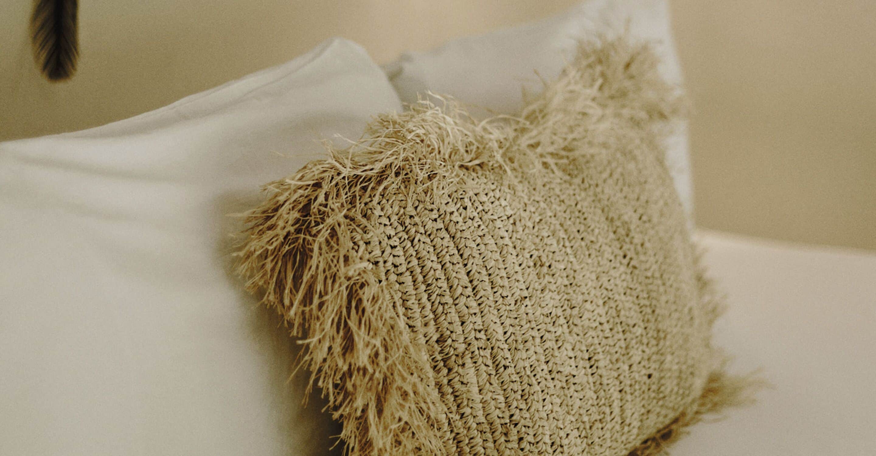 Un gros plan d’un coussin beige à la texture particulière, posé sur un lit.