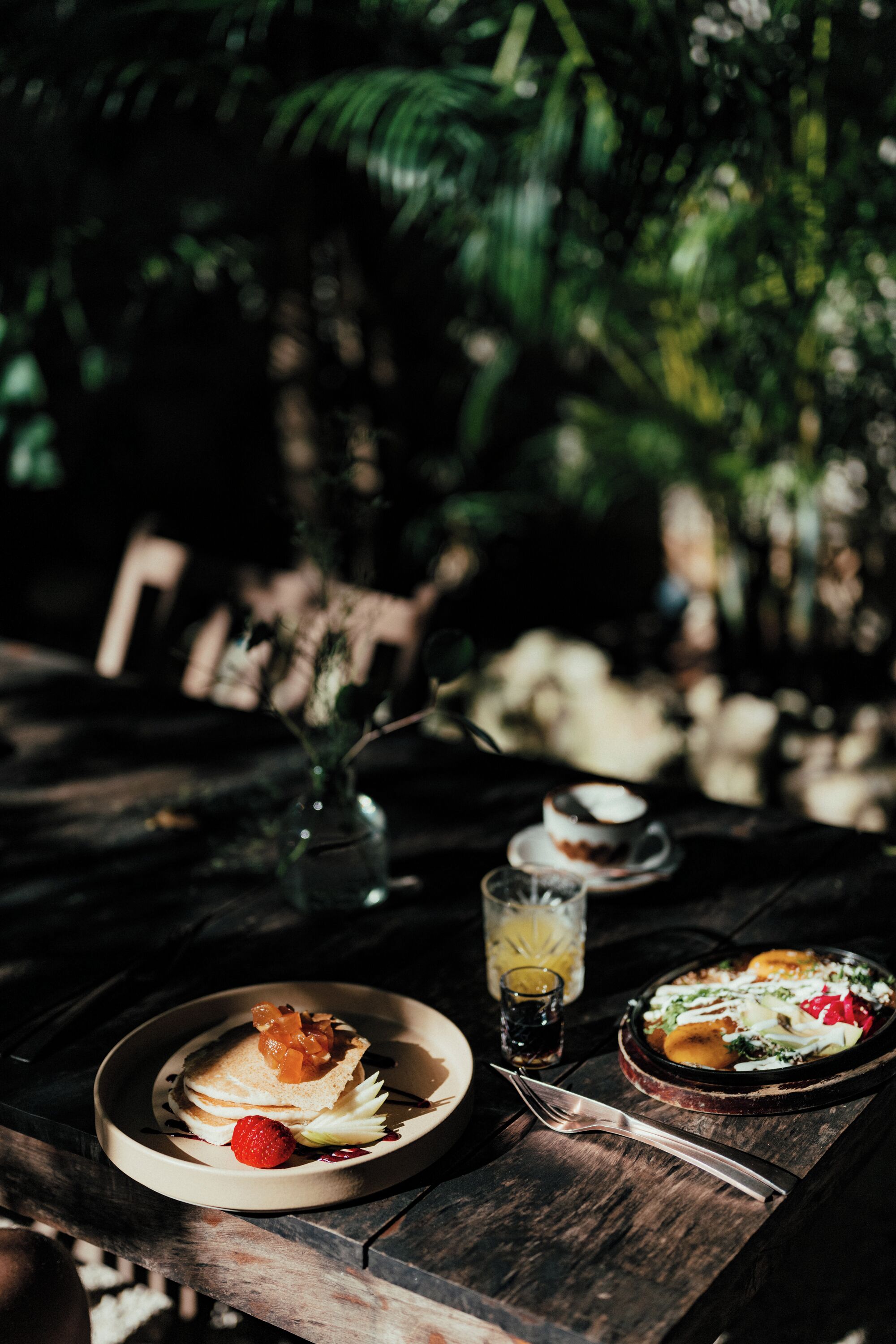 A wooden table with plates of food, a glass of drink, and a fork.