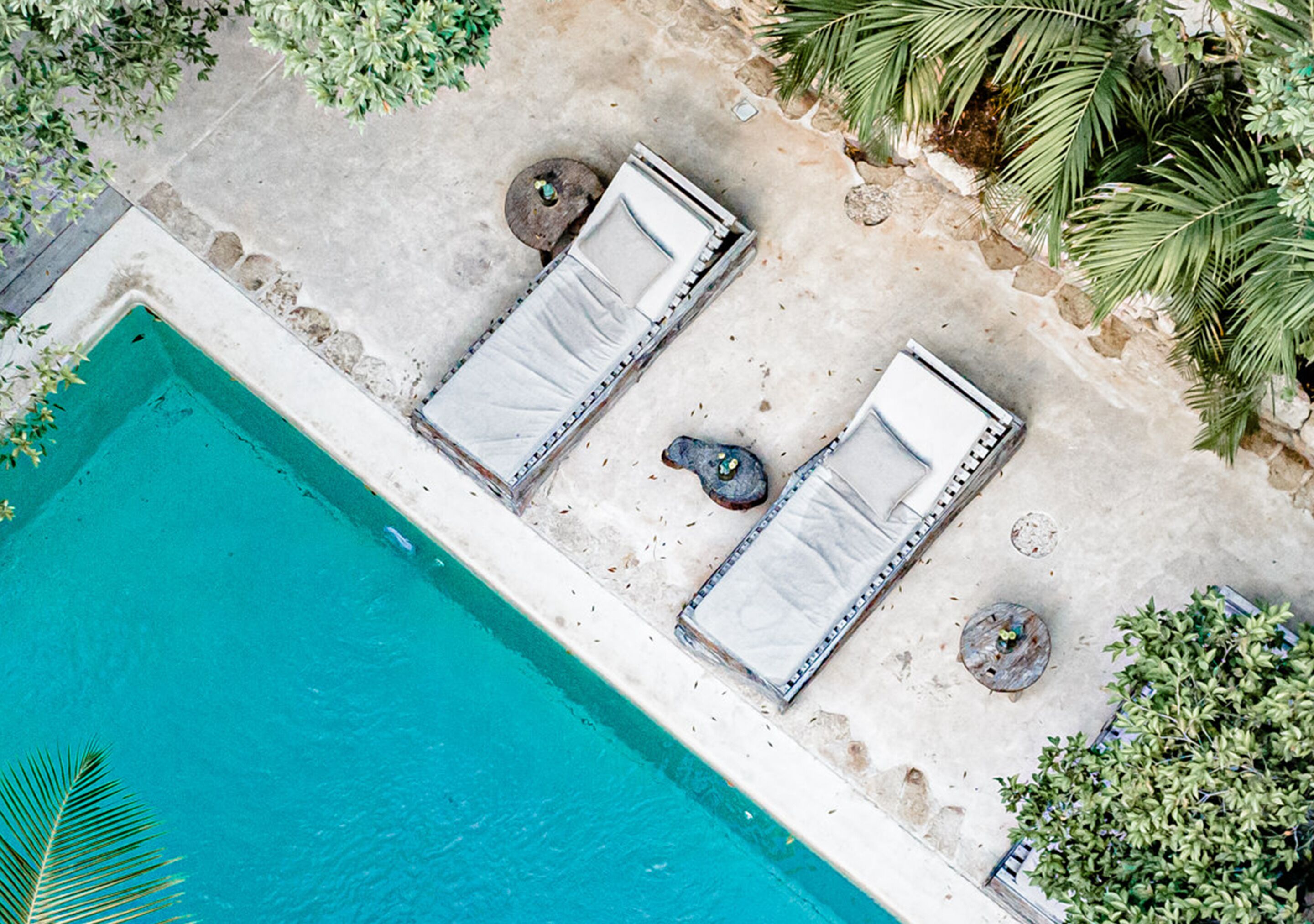 An aerial view of a poolside area with two sun loungers, a small round table, and a stone planter.