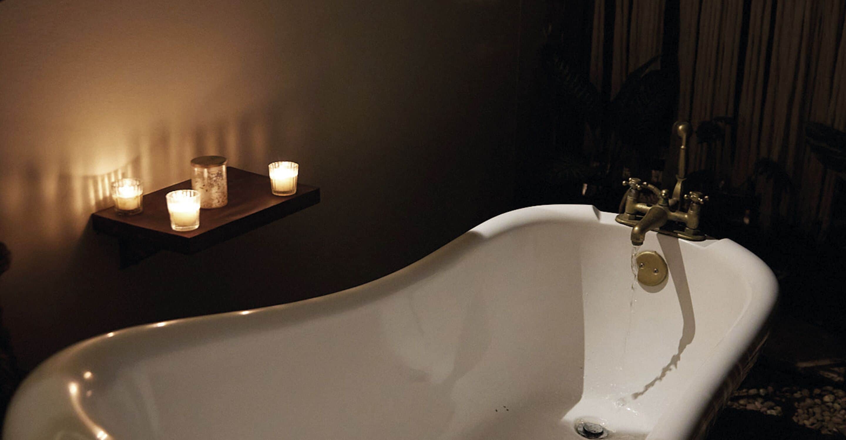 A white bathtub with a single faucet, surrounded by three lit candles on a shelf.