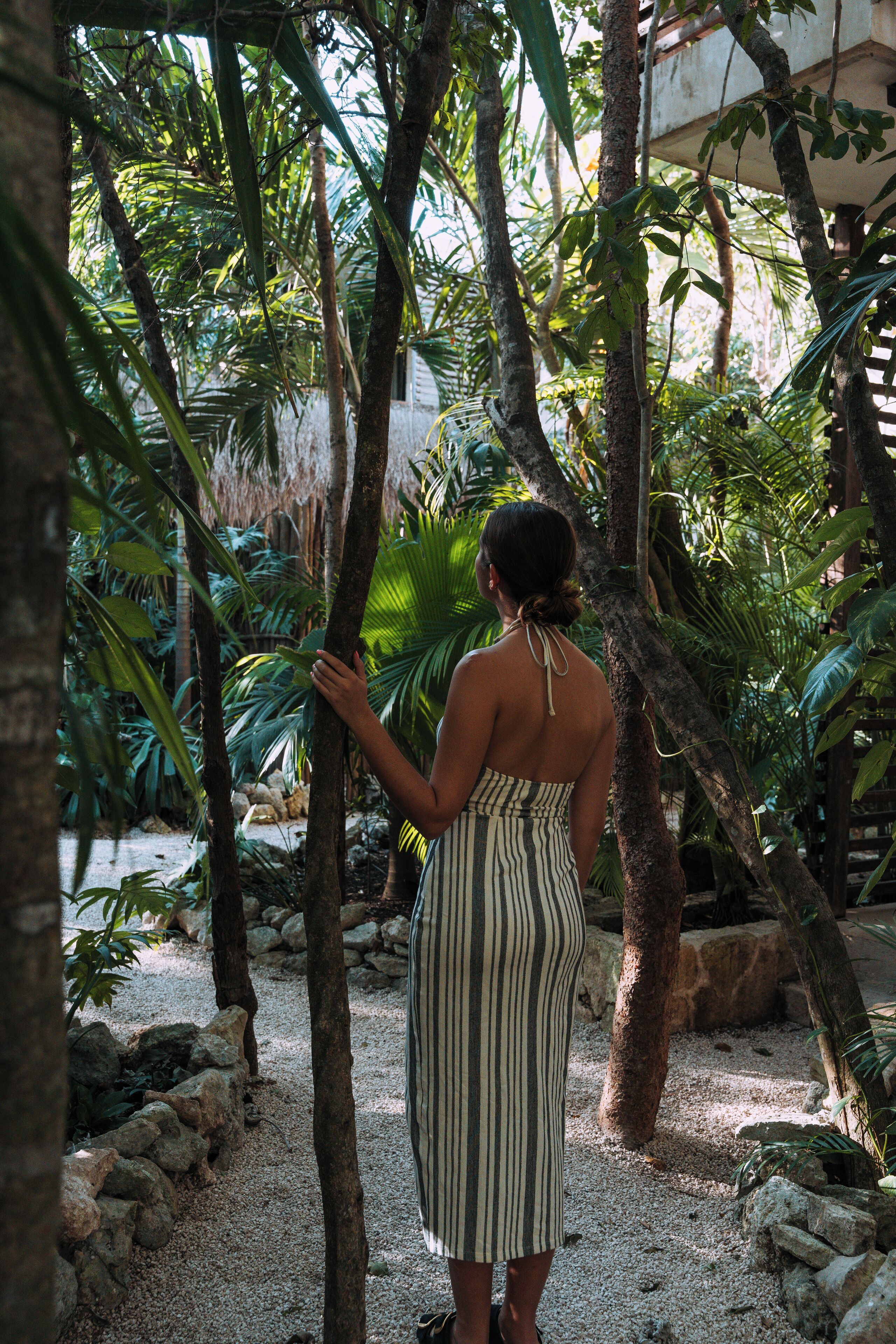 A woman standing in a tropical garden with palm trees and a gravel path.