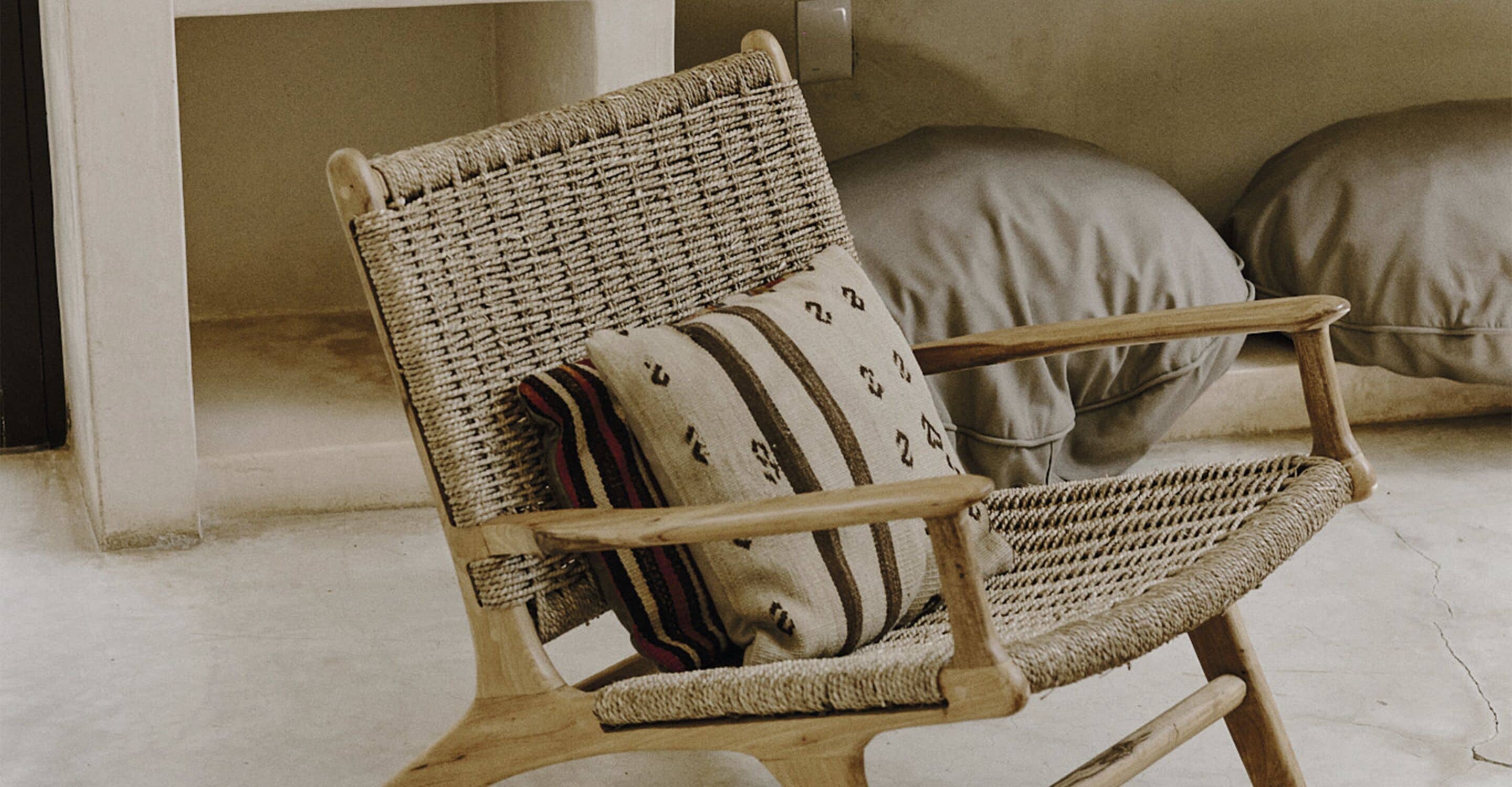 A wicker chair with a striped pillow, positioned in a room with a concrete floor and a plain wall.