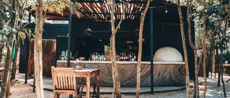 An outdoor seating area with a wooden table and chair, a bar with a counter and bottles, and a large dome structure.
