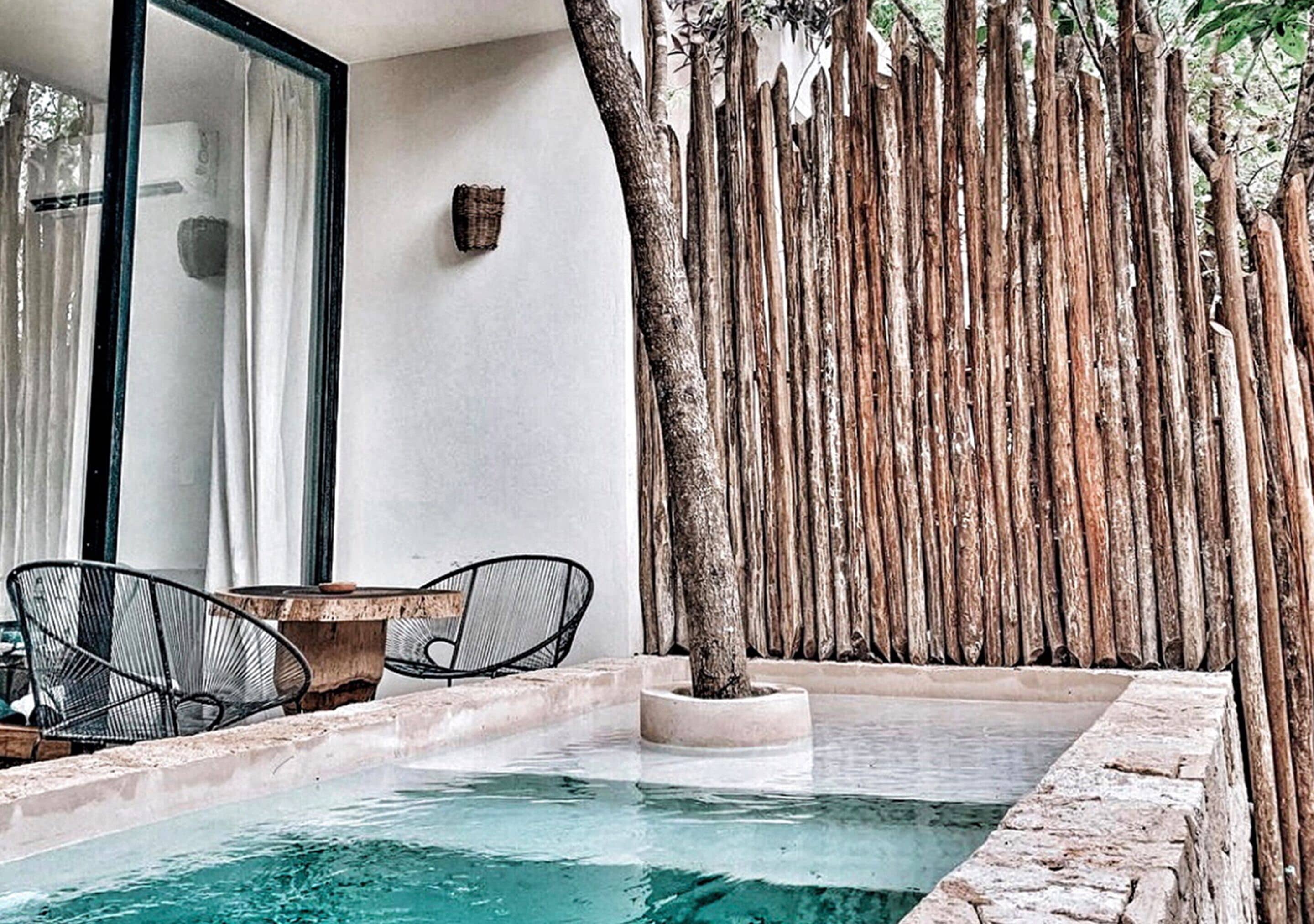 A pool area with a wooden fence, a table with chairs, and a tree.