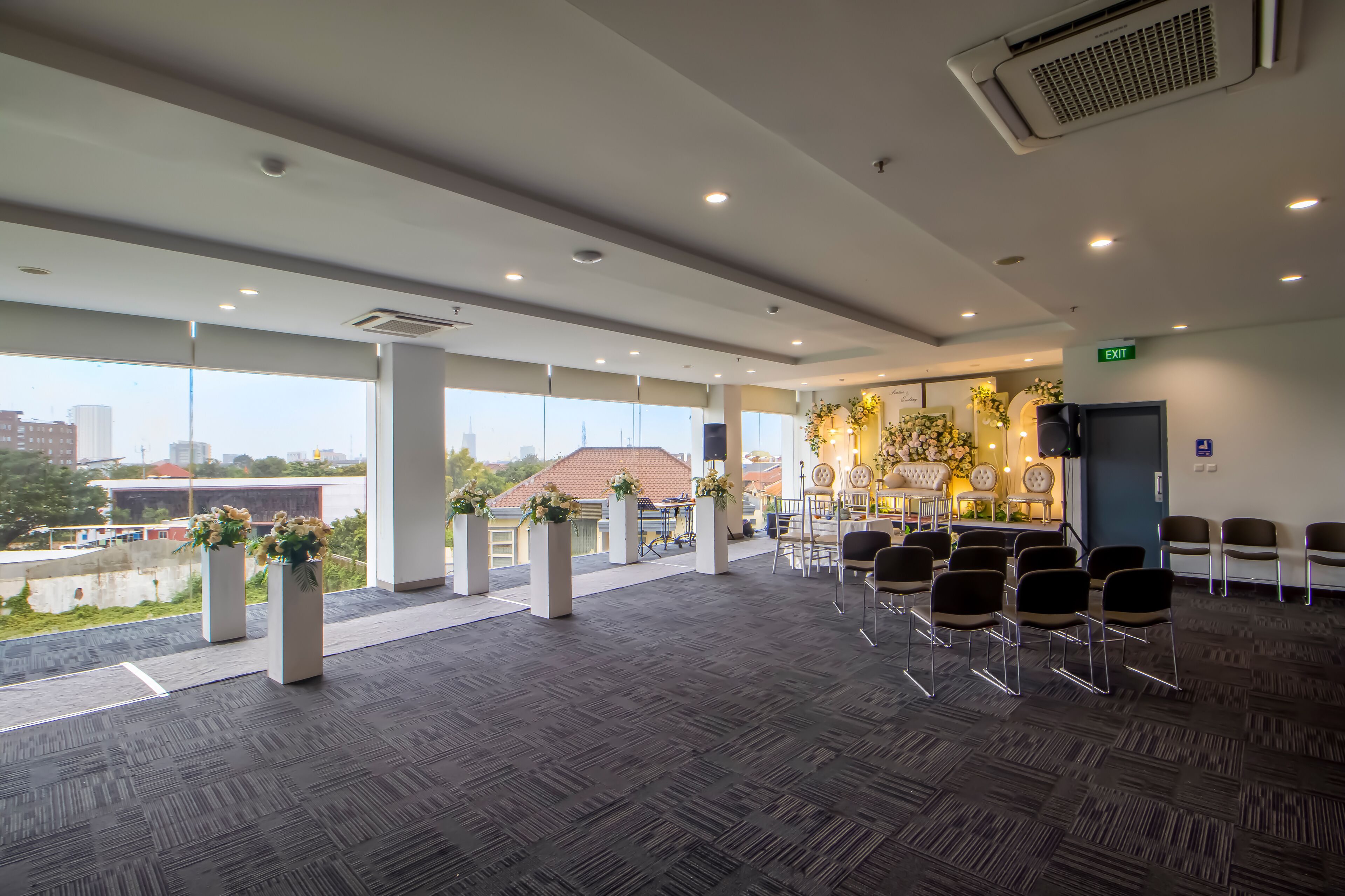 A spacious indoor area with a carpeted floor, large windows, and several chairs arranged for seating.