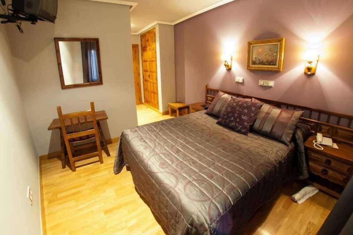 A bedroom with a bed, bedside tables, a chair, a desk, and a mirror.