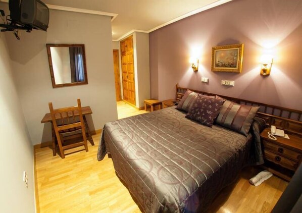 A bedroom with a bed, bedside tables, a chair, a desk, and a mirror. - Hostal Gran Duque (Piedrahita)