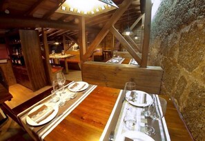 A wooden dining table set with plates, cutlery, and wine glasses, with a rustic stone wall and wooden beams in the background. - Hostal Gran Duque (Piedrahita)