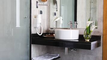 Un baño moderno con cabina de ducha de vidrio, un lavabo blanco, un espejo y un florero con flores.