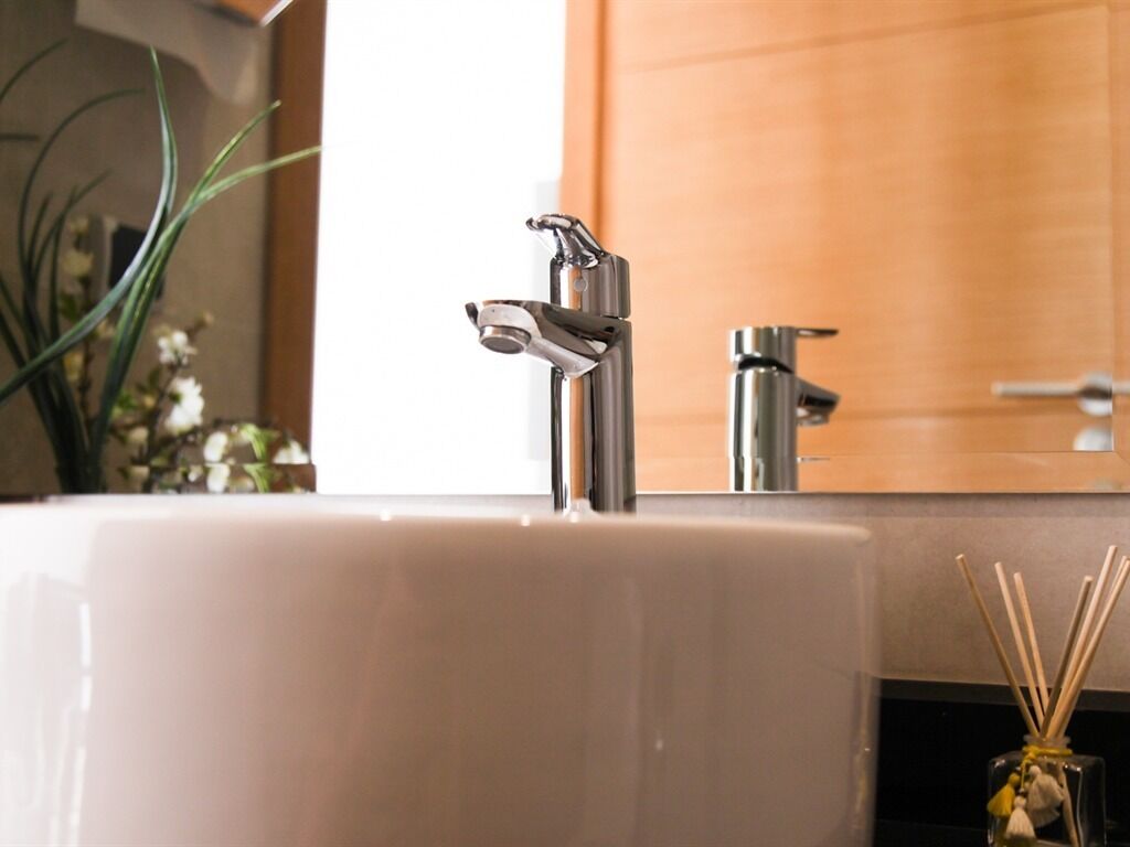 A bathroom sink with a modern faucet and a glass jar with reed sticks.