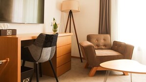 A hotel room with a flat-screen TV, a desk with a chair, a sofa, a lamp, and a window with curtains. - Smarts Hotel (Rabat)