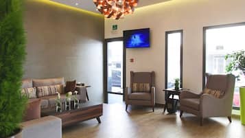 Een moderne lobby met een bank, fauteuils, een salontafel, een televisie en een grote plant.