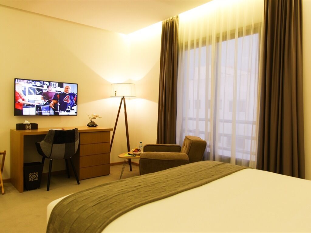 A hotel room with a bed, a desk with a chair, a TV, and a lamp.