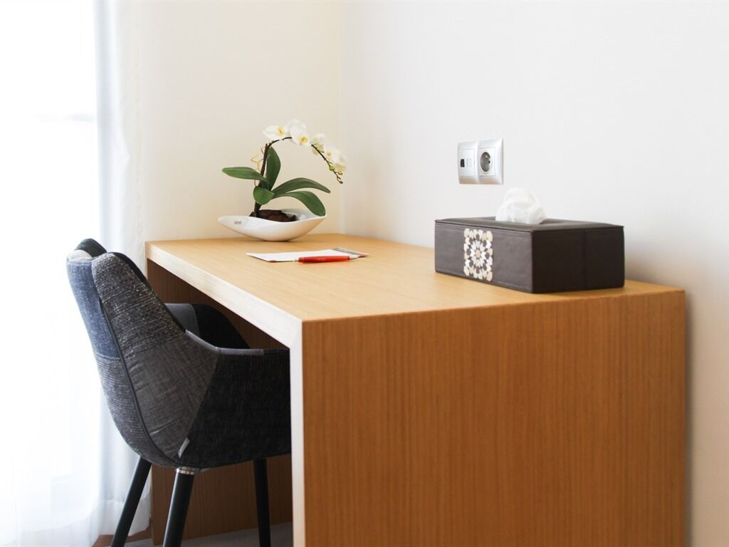 A wooden desk with a white bowl containing a plant, a tissue box, and a red pen.