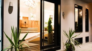 A hotel entrance with a modern design, featuring a glass door, a reception desk, and potted plants. - Smarts Hotel (Rabat)