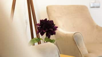 Une pièce avec un fauteuil beige, une petite table et une plante en pot ornée de fleurs d’un violet foncé.