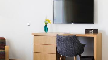 A modern room with a wooden desk, a black chair, a flat-screen TV mounted on the wall, and a vase with yellow flowers on the desk.