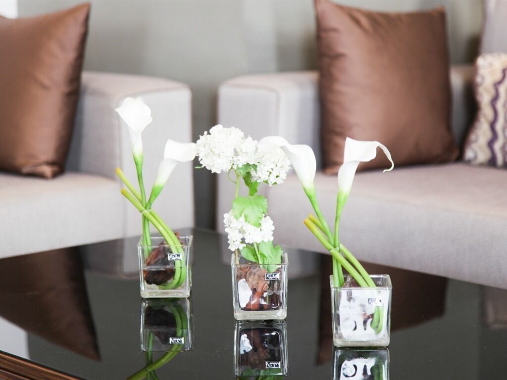 Tre glasvaser med blommor placerade på en reflekterande yta.