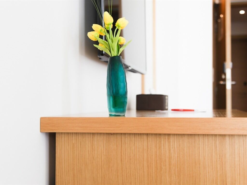 A reception desk with a vase of yellow flowers, a black object, and a red item on the counter.