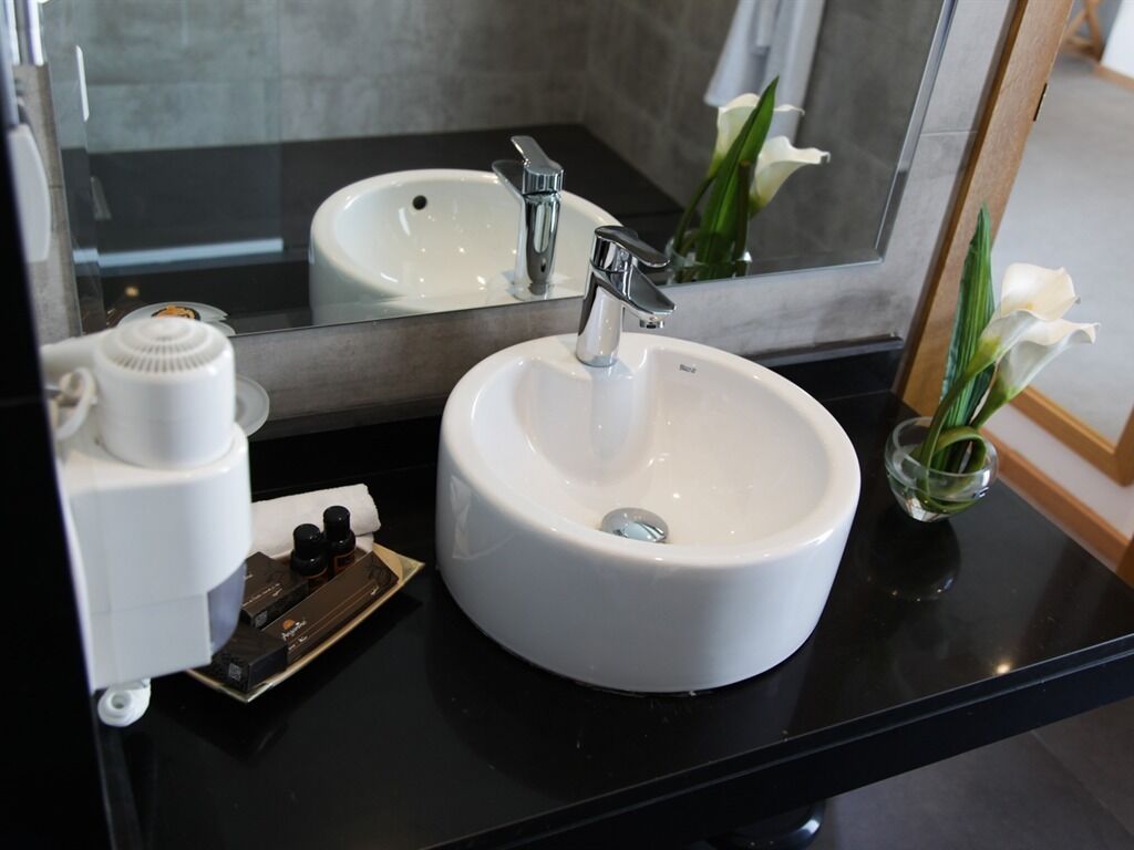 A bathroom with a white sink, a mirror, and a small vase with white flowers.