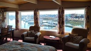 Une chambre avec un lit, deux fauteuils, une petite table et une vue sur un port de plaisance avec des bateaux et des bâtiments.