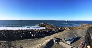 A coastal road with a rocky breakwater, a parked car, and a distant ship. - Islander Westport (Westport)