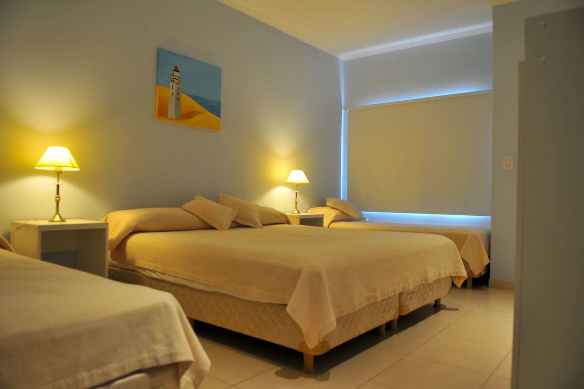 Ein Hotelzimmer mit zwei Betten, jeweils einem Nachttisch und einer Lampe, einem Gemälde an der Wand und einem Fenster mit Jalousien.