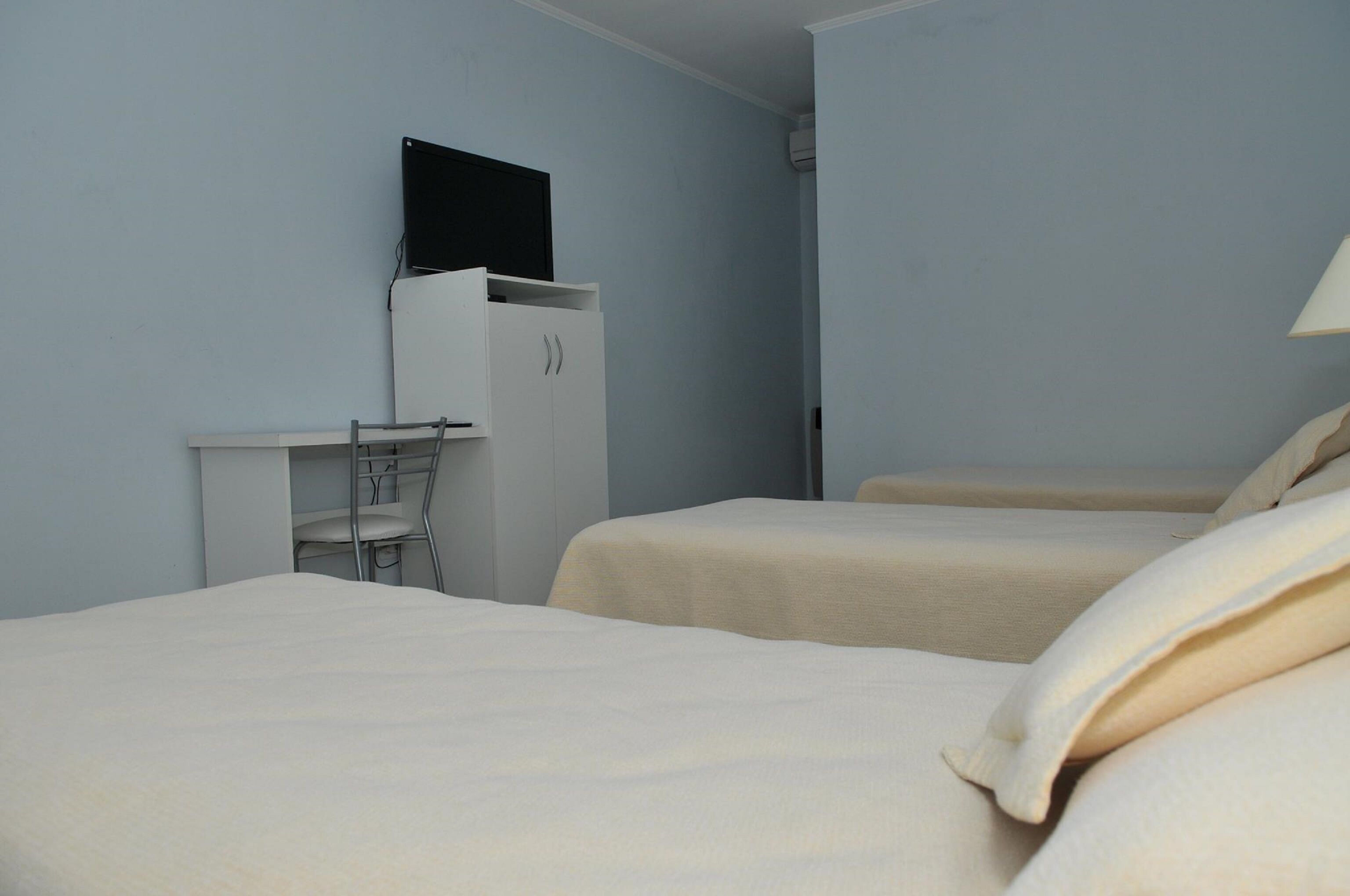 A hotel room with two beds, a desk, and a TV mounted on the wall.