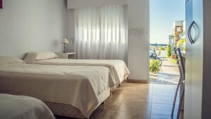 Ein Hotelzimmer mit zwei Betten, einem Fenster mit durchsichtigen Vorhängen, einer Lampe und Blick auf den äußeren Balkon.