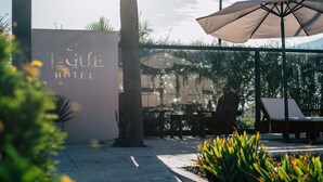 Außenbereich des TAGUE HOTEL mit Glaswand, Palmen und einer Person im Hintergrund.