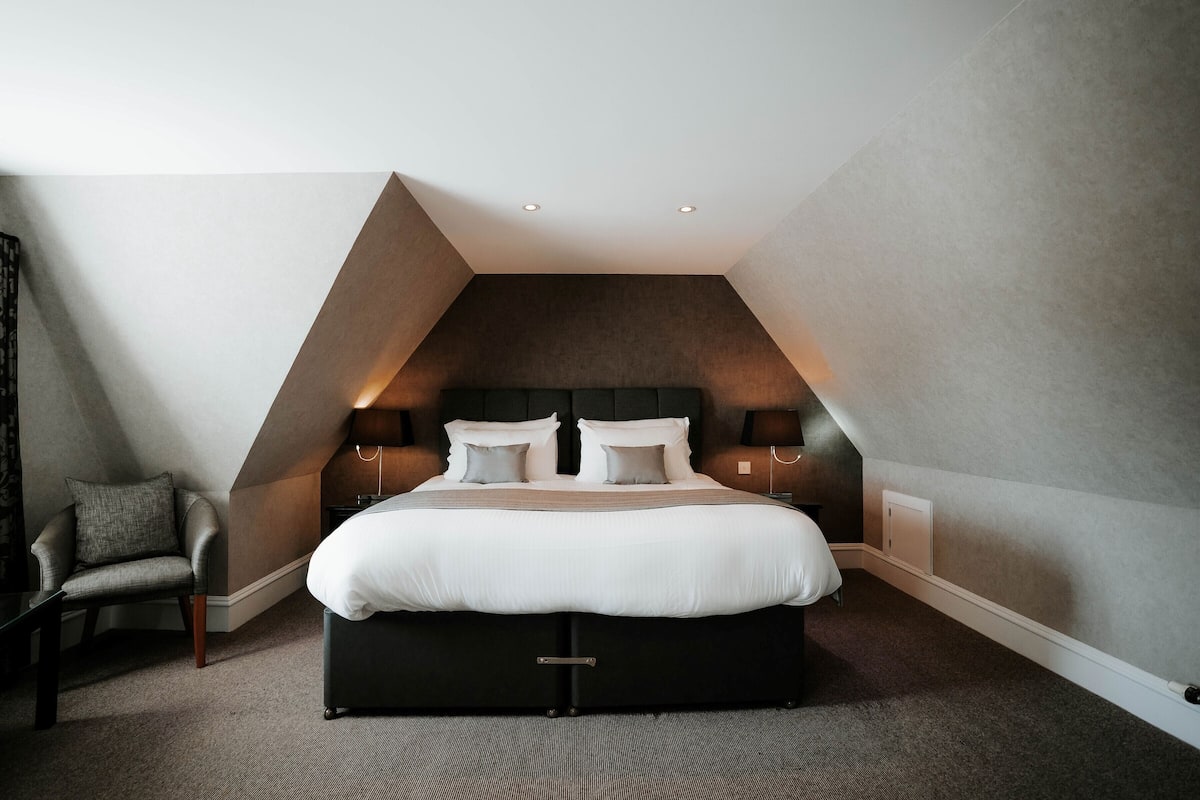 Ein modernes Schlafzimmer mit einem großen Bett, zwei Nachttischen, einem Sessel und einer schrägen Decke.
