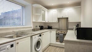 A modern kitchen with white cabinetry, a stainless steel sink, a washing machine, an oven, and a microwave. - New Inn Hotel (Ellon)