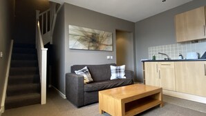 A modern living room with a grey sofa, a wooden coffee table, and a staircase leading to a second floor. - New Inn Hotel (Ellon)