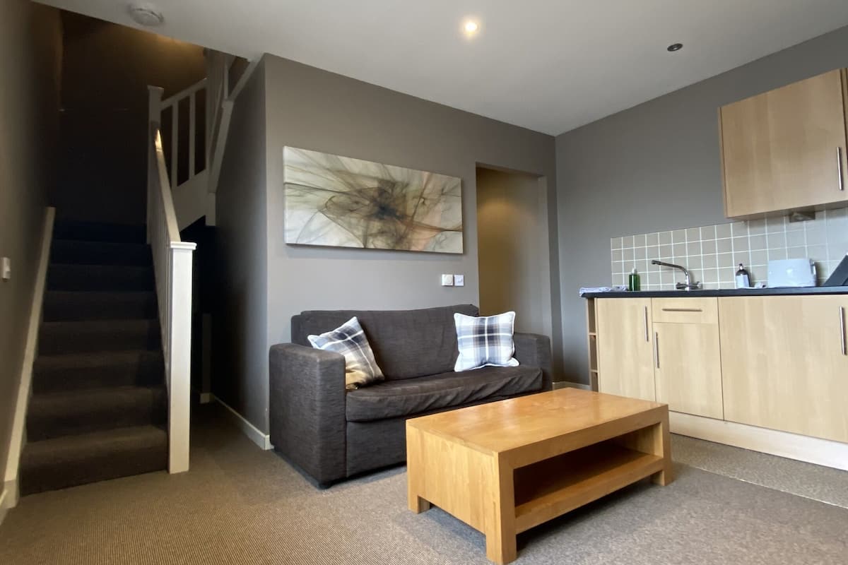 Ein modernes Wohnzimmer mit einem grauen Sofa, einem Holztisch und einer Treppe, die zu einer zweiten Etage führt.