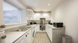 A modern kitchen with white cabinets, stainless steel appliances, and a window with blinds. - New Inn Hotel (Ellon)