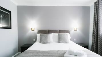 A neatly made bed with a grey quilt, two bedside tables with lamps, and a grey curtain on the window.