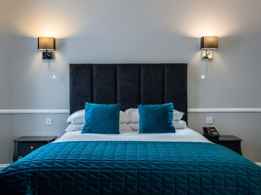 Habitación de hotel con una cama grande, dos mesitas de noche, un teléfono e iluminación en la pared.