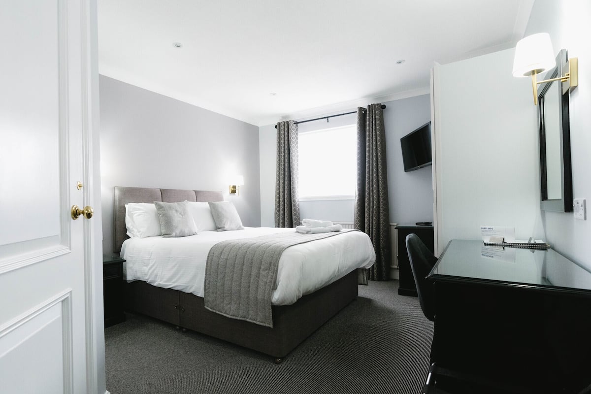 Ein Hotelzimmer mit einem Bett, einem Schreibtisch, einem Stuhl, einem Fernseher und einem Spiegel.
