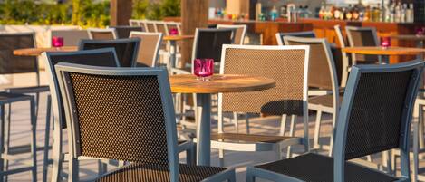 Outdoor seating with tables and chairs, a bar area, and a television screen in the background.