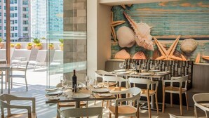 A restaurant with outdoor seating, a mural of seashells and starfish, and a view of a cityscape. - Fiesta Inn Puerto Vallarta Isla (Puerto Vallarta)