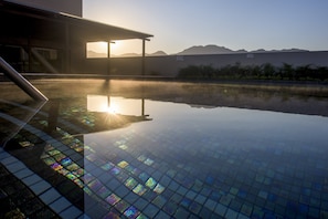 A clear pool with a tiled floor, a covered area, and mountains in the background.